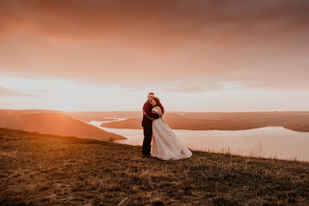 A loving couple wedding newlyweds walk in summer in the fall on mountain on cliff above the river