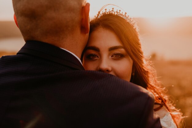 A loving couple wedding newlyweds in white dress and suit walk hug kissing whirl on tall grass in summer field on mountain above the river