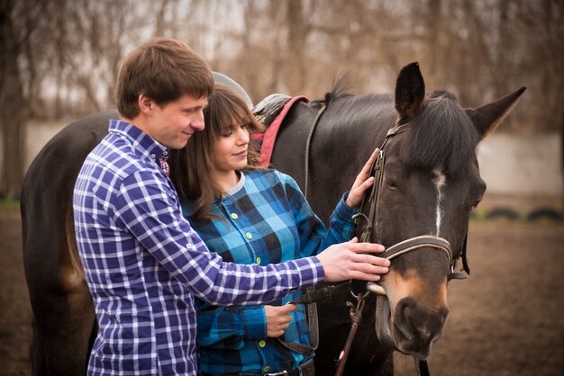 Loving couple with a horse on a ranch in an autumn cloudy day.