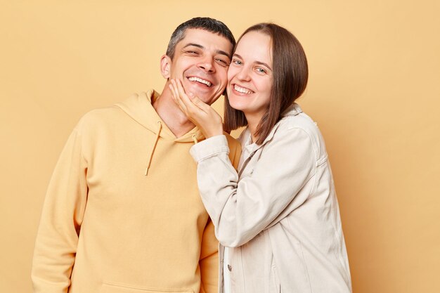 Loving couple woman and man wearing casual style clothing standing isolated over beige background looking at camera with love and gentle spending romantic time together