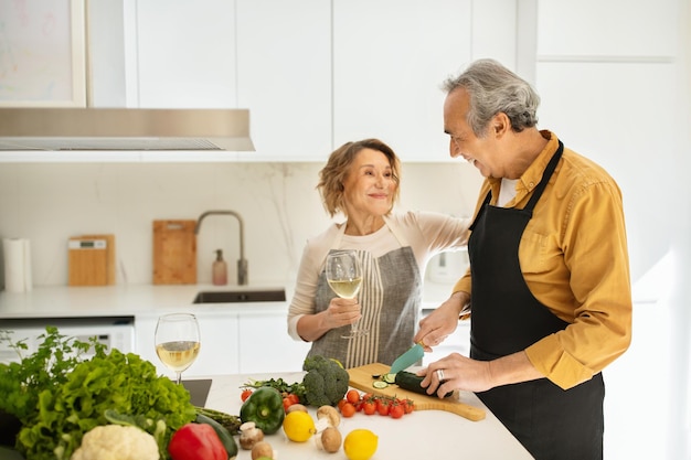 Loving happy senior spouses celebrating marriage anniversary talking man making dinner and woman