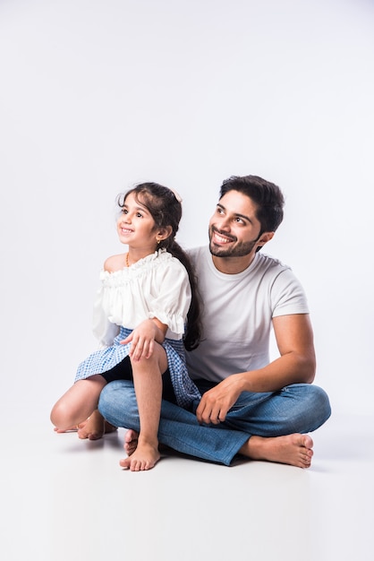 Loving Indian daddy embracing cute little adorable daughter sitting over lap or piggyback - concept showing love, care, closest person, fathers day