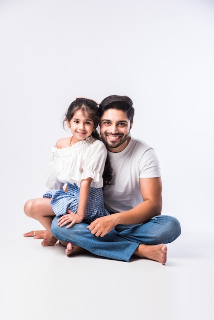 Loving Indian daddy embracing cute little adorable daughter sitting over lap or piggyback - concept showing love, care, closest person, fathers day