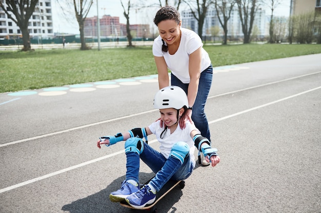 Loving mother behind her son, who sits on a skateboard