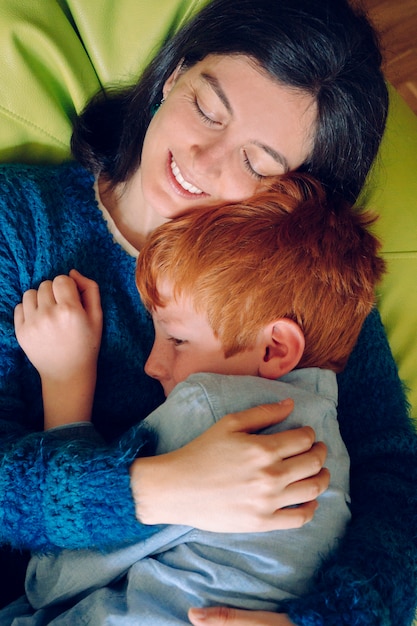 Loving mother hugging her son being playful. Childhood concept. Single woman playing with his child at home. Family lifestyle inside the house with children. Entertainment for little kids indoors.