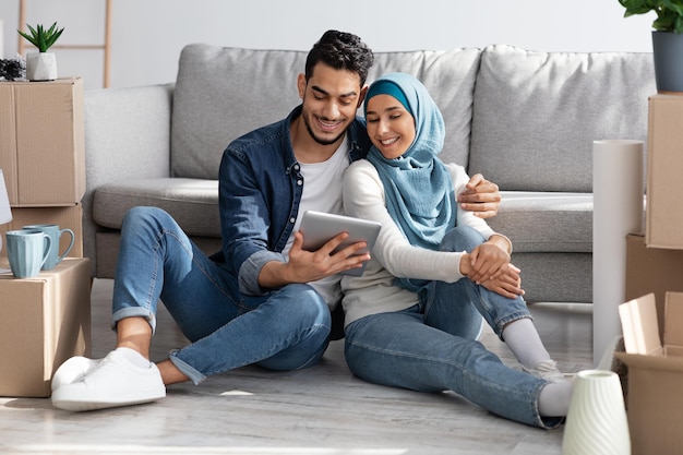 Loving muslim family sitting on floor with tablet among boxes