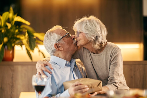 A loving senior couple is hugging and kissing and holding a gift on valentines day