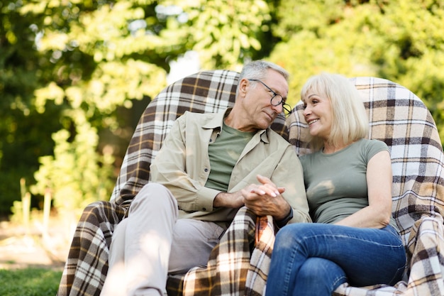 Loving senior married couple resting in their garden in countryside sitting in wicker chairs and