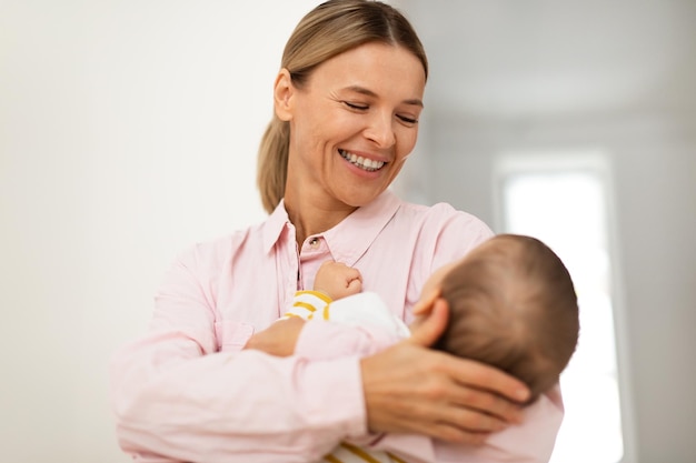 Loving smiling mother lulling her baby daughter to sleep carrying her in arms standing in bedroom