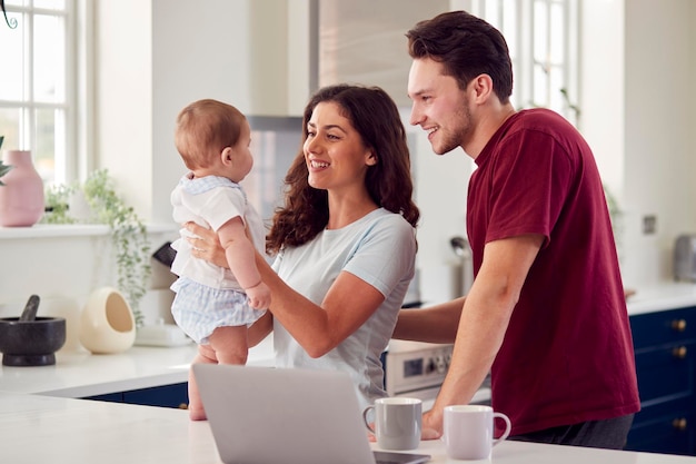 Loving Transgender Family With Baby At Home Together Looking At Laptop On Kitchen Counter