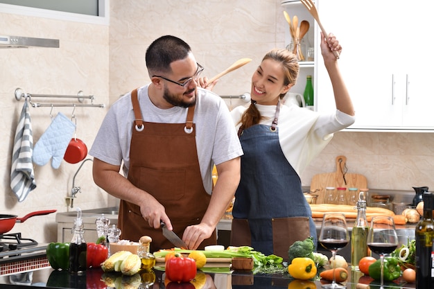 Loving young Asian couple cooking in kitchen making healthy food together feeling fun