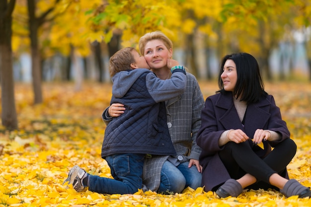 Loving young boy kissing his mother as he relaxes in an autumn park with the family sitting on colorful yellow leaves in a tender portrait