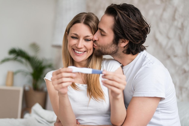 Loving young couple feeling happy about positive pregnancy test kissing and hugging at home