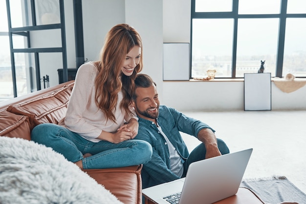 Loving young couple using laptop and smiling while spending time at home