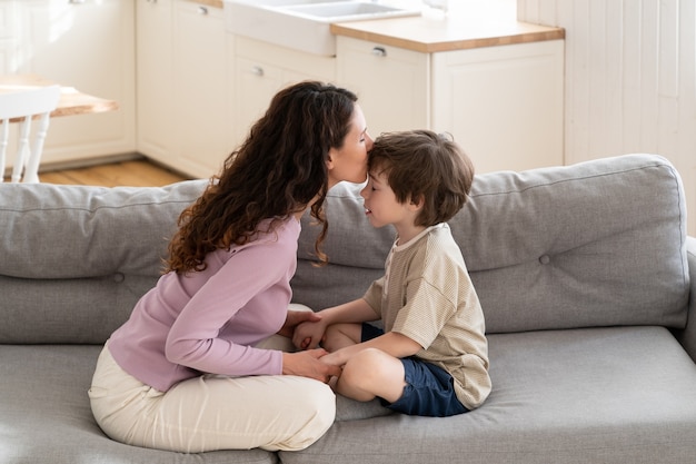 Loving young mom kissing child in forehead tender relationship between parent and preschool boy kid