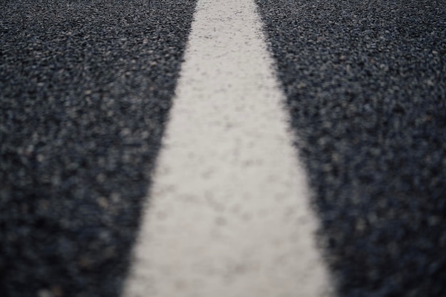 Low angle closeup of a white paint line on the center of a black asphalt road