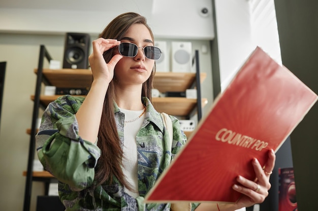 Low angle funky young woman holding vinyl record in music store