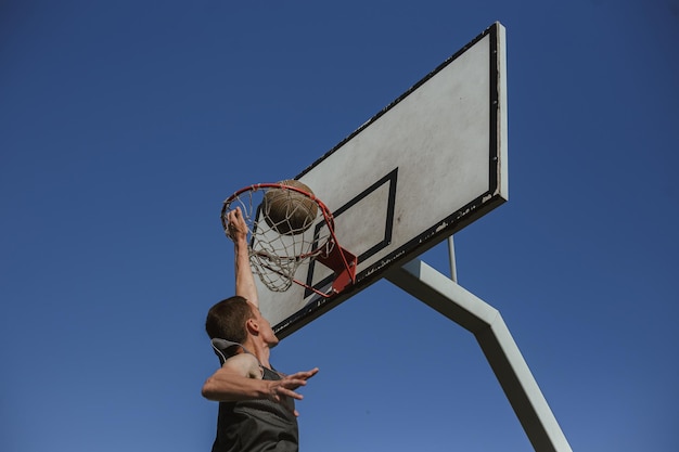 Low angle of man playing basketball and throwing ball in hoop on playground in summer