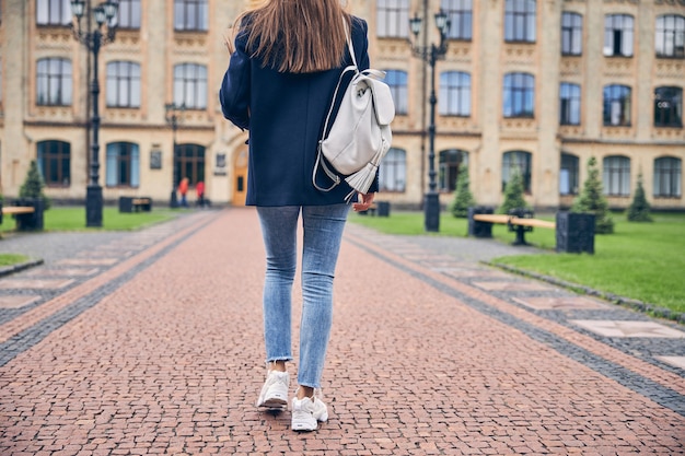 Low angle photo of brunette woman with backpack in casual clothes going alone to university