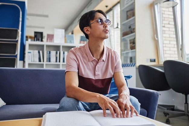 Low angle portrait of asian young man reading book in tactile braille font in college library copy s