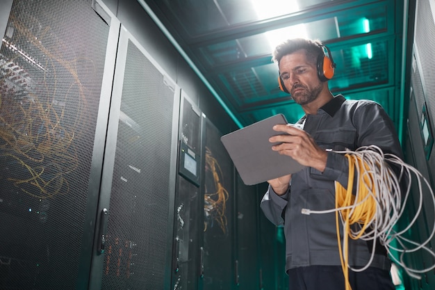 Low angle portrait of network engineer using tablet in server room during maintenance work in data center, copy space