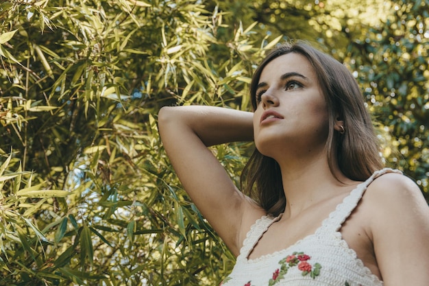 Low-angle shot of an attractive girl with brown long hair posing in front of the tree branches