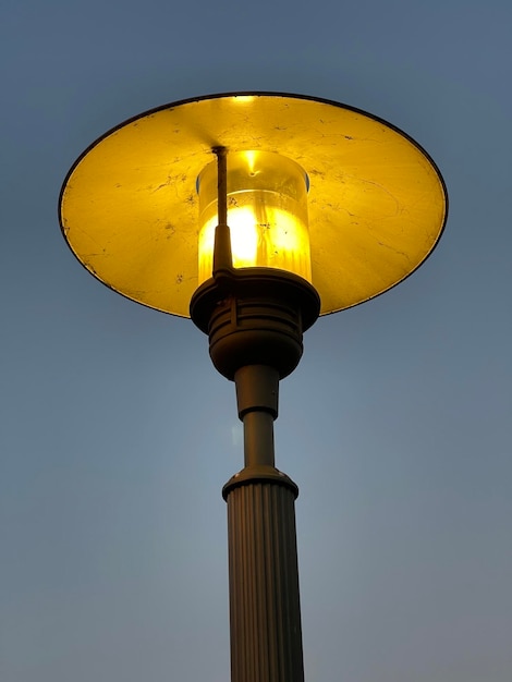 Low angle shot of a beautiful street lamp glowing with warm yellow light against dusk sky