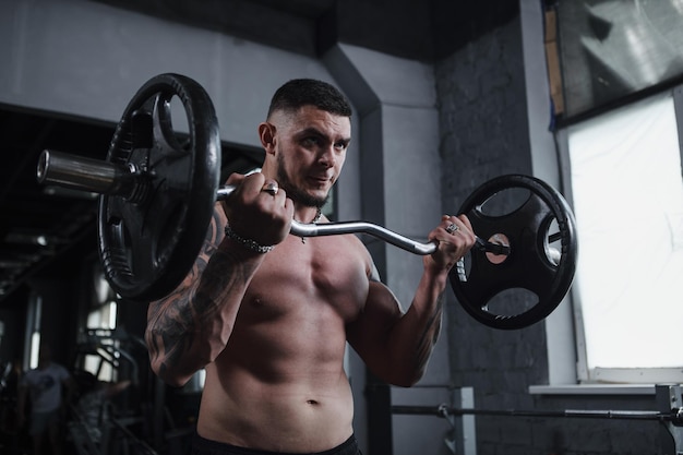 Low angle shot of a handsome ripped tattooed male athlete working out with barbell looking focused