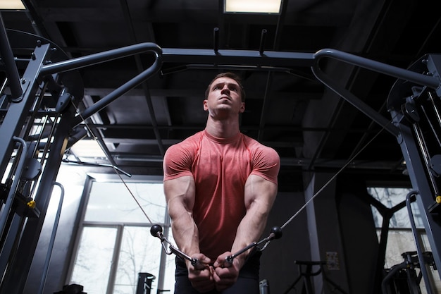 Low angle shot of a muscular athlete exercising in cable crossover gym machine