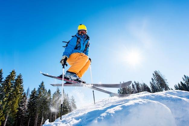 Low angle shot of a skier in colorful gear jumping in the air while skiing on a slope