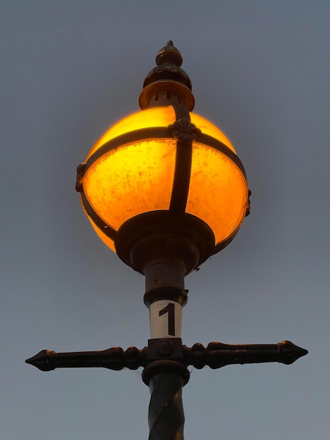 Low angle shot of a vintage street lamp glowing orange against evening sky