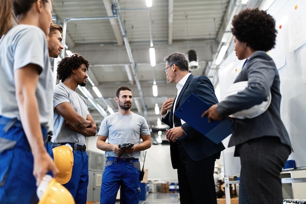 Low angle view of businessman talking with team of manual workers while having staff meeting in industrial plant