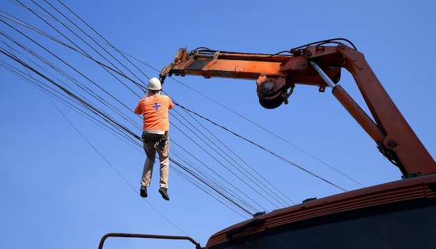 Low angle view of crane truck lifting electrician to clearing messy electric lines on the street