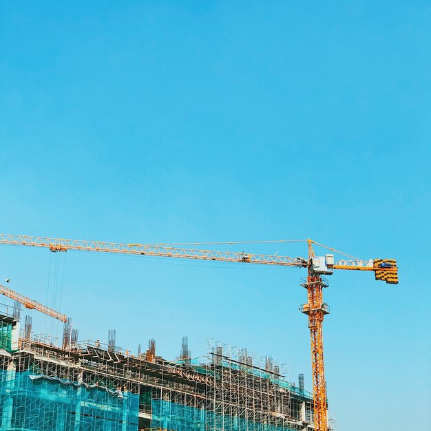 Low angle view of cranes at construction site against sky