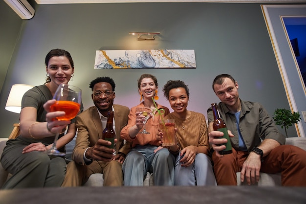 Low angle view at diverse group of friends cheering to laptop screen while celebrating online together in home setting