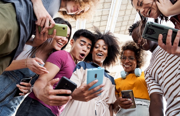 Low angle view of a group of young teenagers holding cell phones. Surprised faces looking at the screen. Concept of technology, connection, colorful.