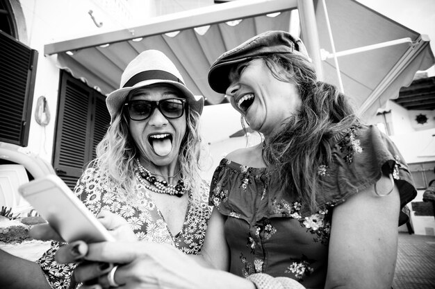 Photo low angle view of happy friends using smart phone while sitting against built structure