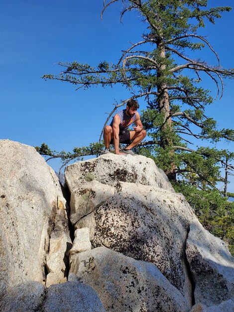 Low angle view of man sitting on rock against sky