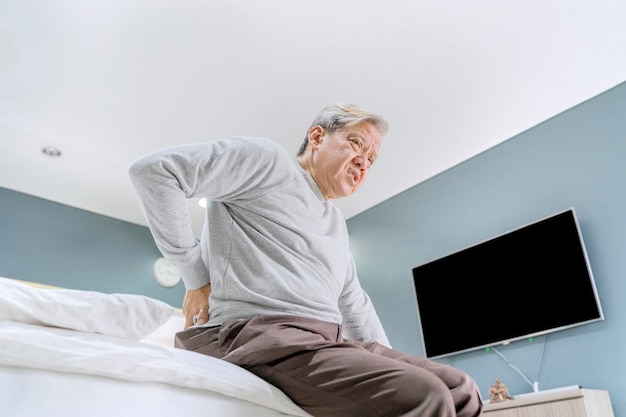 Photo low angle view of senior man with backache sitting on bed at home