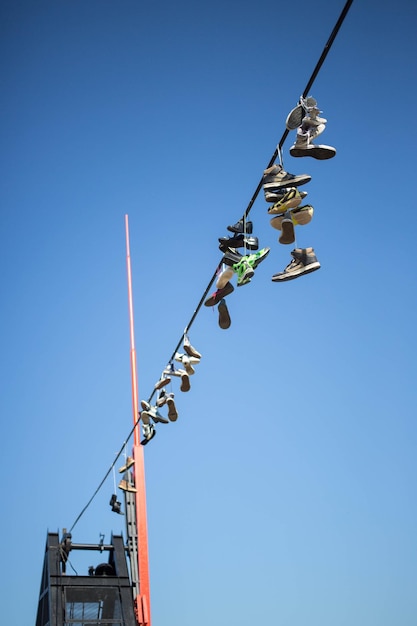 Low angle view of shoes hanging from power cable against clear blue sky