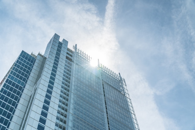 Low angle view of a skyscraper with sun and cloudscape