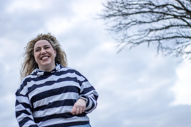 Low angle view of smiling woman walking with sky in background Bottom view of smiling woman in sweater walking outdoors