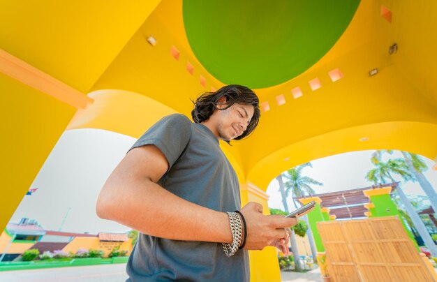 Low angle view of young man using cell phone outdoors Smiling latin guy texting with cell phone in Nagarote park