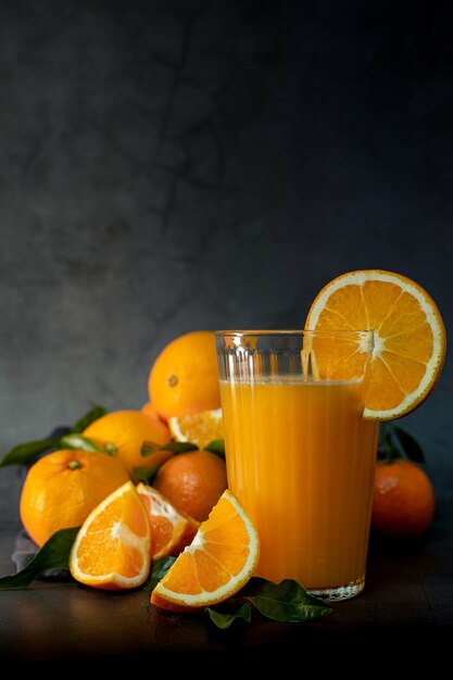 Low key light image of a glass of fresh orange juice next to a set of oranges ready to squeeze