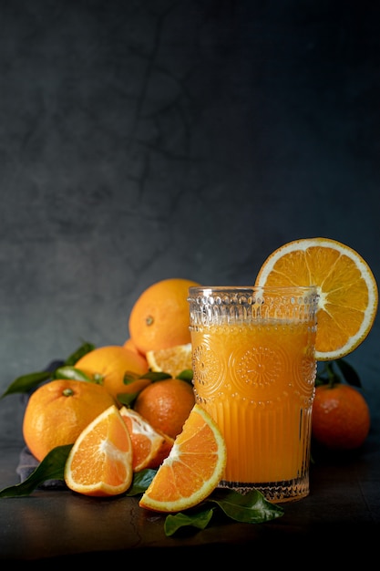 Low key light image of a glass of fresh orange juice next to a set of oranges ready to squeeze