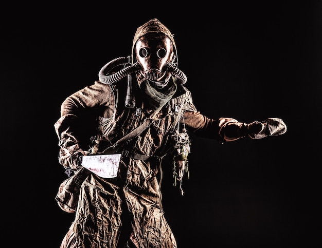 Low key portrait of post apocalyptic creature, living in catacombs mutant, survived in nuclear disaster human in ragged cloth and gas mask, armed with handmade cold weapon isolated on black background