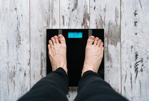 Photo low section of barefoot man standing on a weight scale on wooden floor