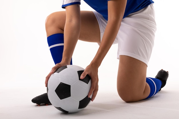 Photo low section of biracial young female player holding soccer ball while kneeling on white background