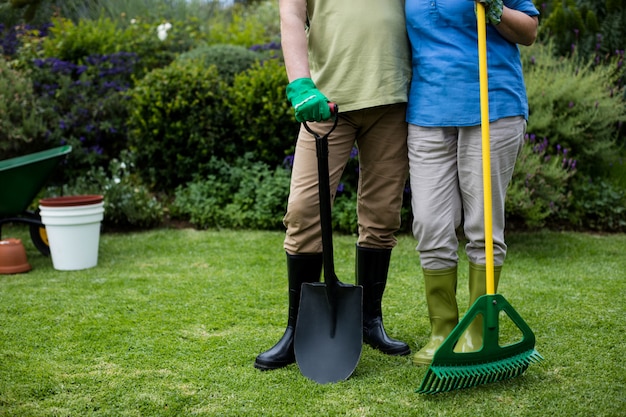 Low section of senior couple standing with garden tools