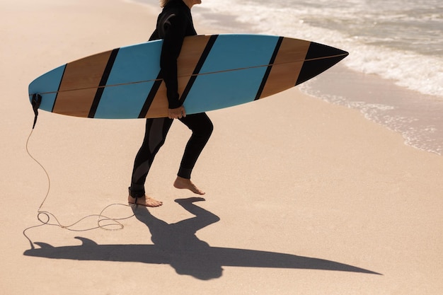 Photo low section of senior female surfer walking with surfboard on the beach